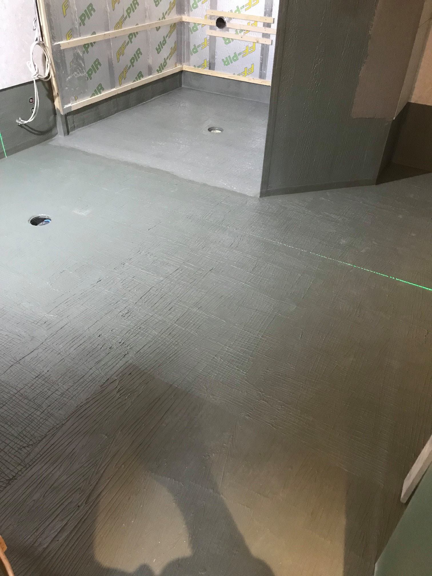 Harmaa lattia, jossa on vihreä laserlinja, ja osittain rakennettu suihkutila, jossa on FF-PIR-eristyslevyt.