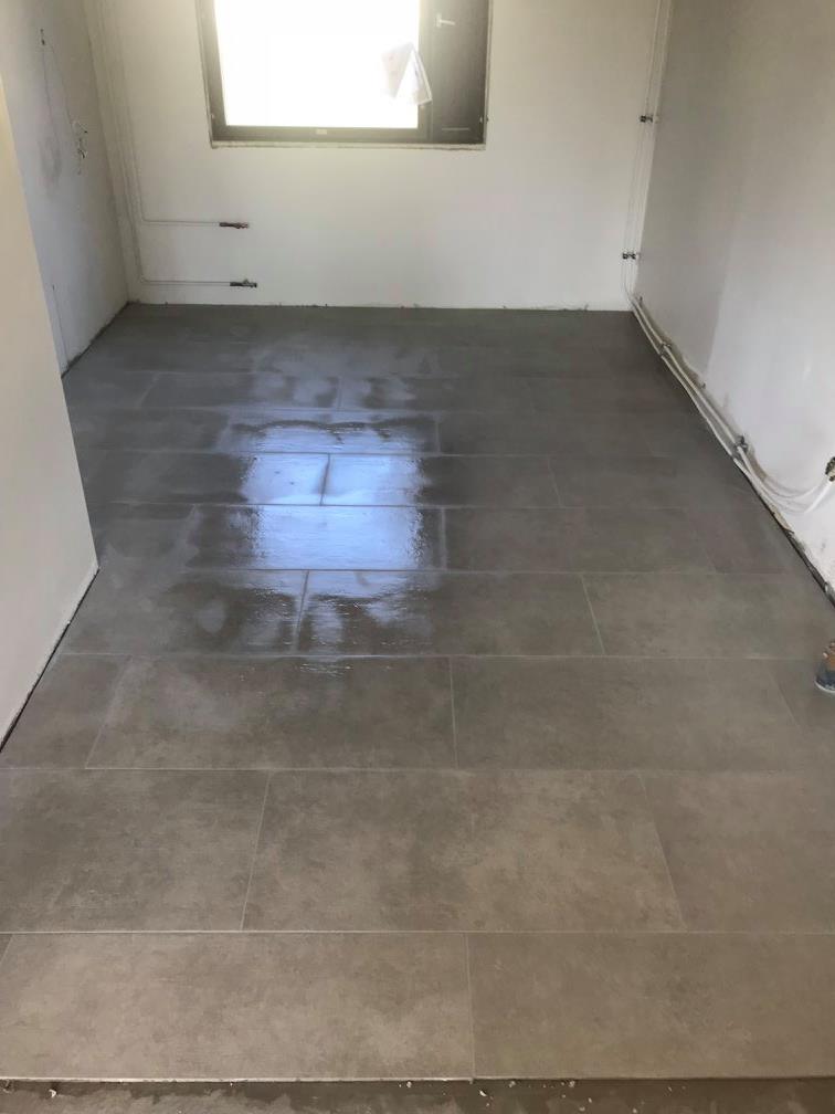 Huone, jossa on harmaat lattialaatat, valkoiset seinät ja ikkuna, jossa on valoisa heijastus.