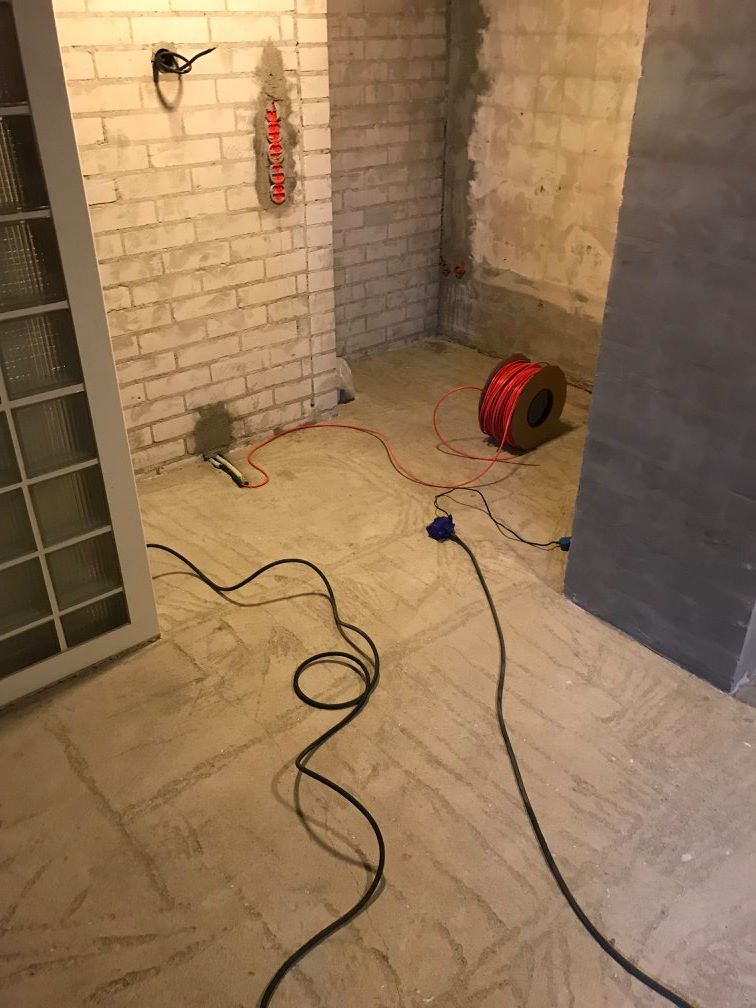 Keskeneräinen huone, jossa on punainen kaapelikela, musta johto, valkoiset tiiliseinät ja avoin ovi.