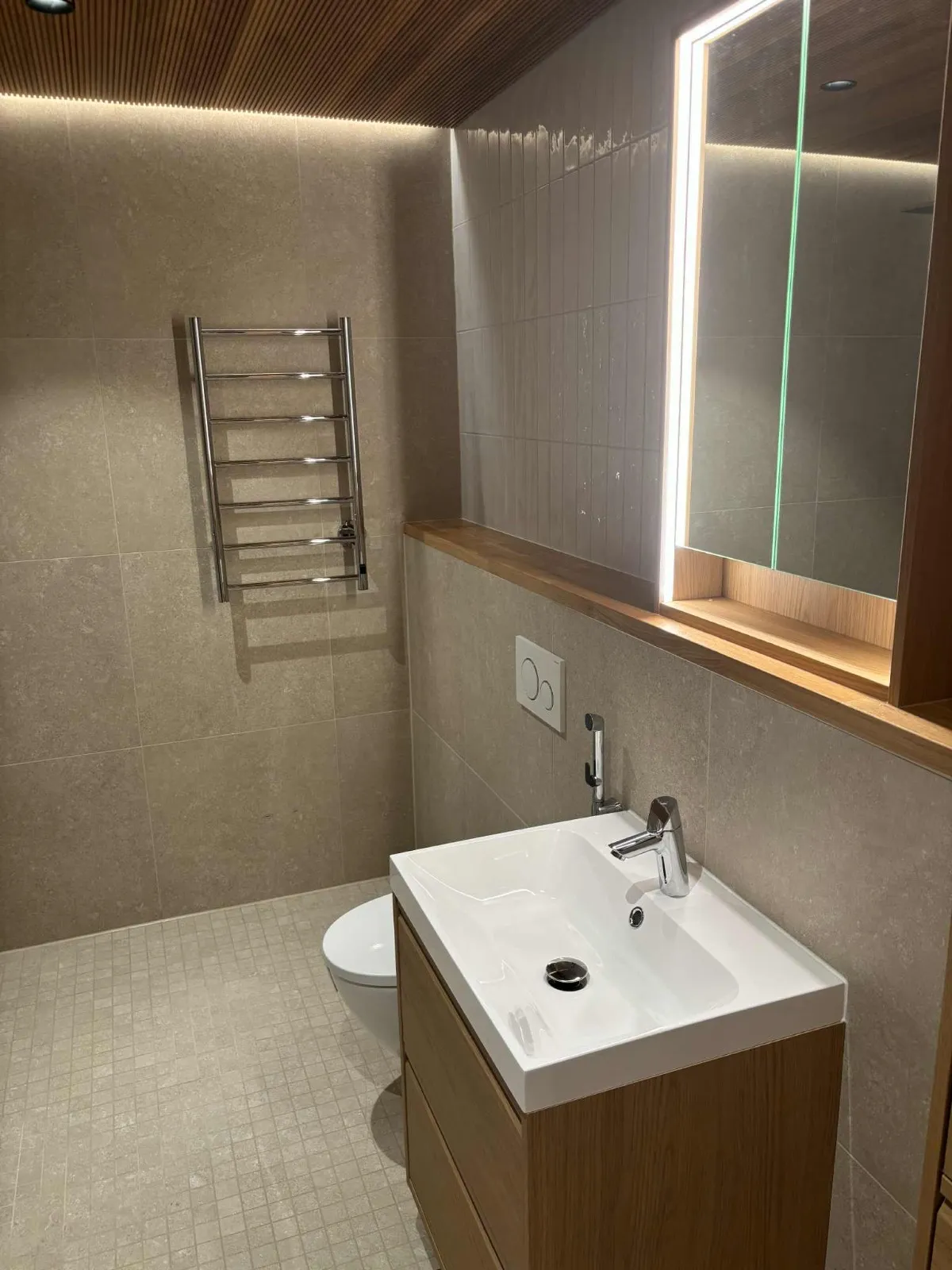 Moderni kylpyhuone, jossa on puinen katto, pyyhekuivain, valaistu peili ja puinen pesuallas.