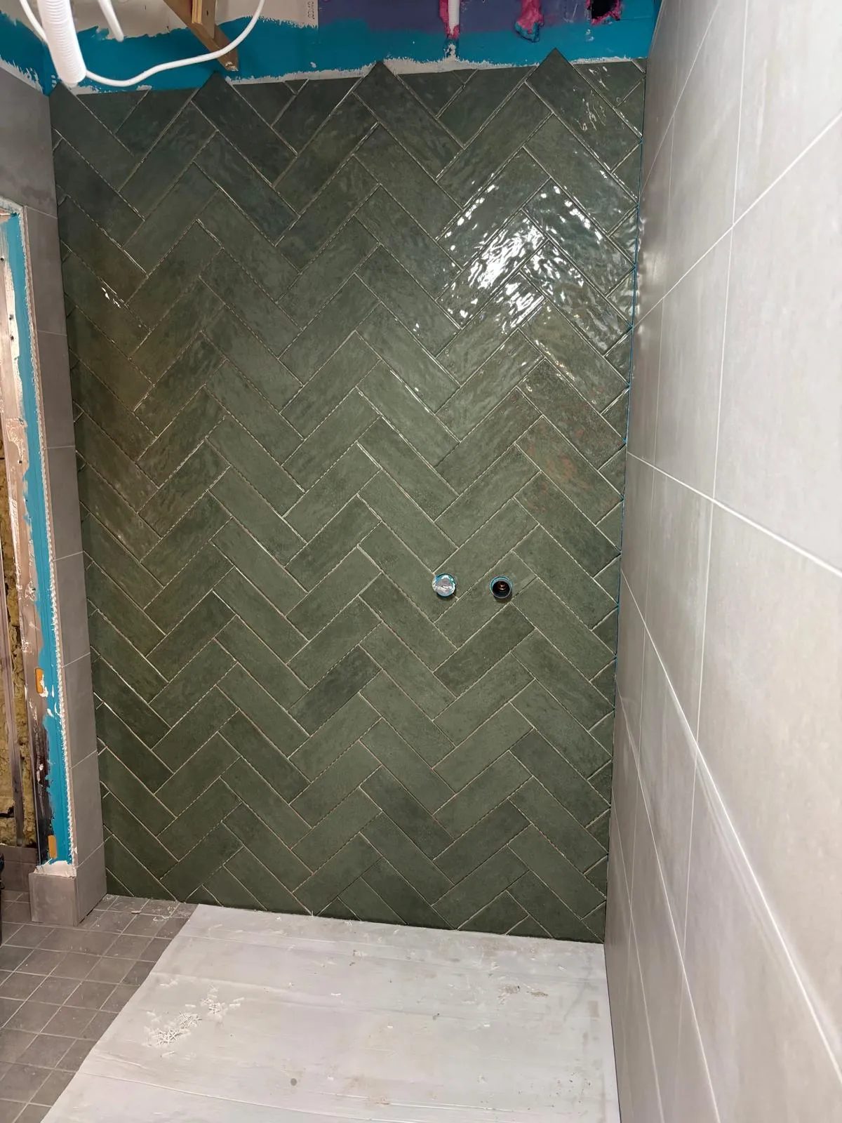 Kylpyhuoneen seinässä on vihreitä kalanruotokuvioisia laattoja ja valkoisia suorakulmaisia laattoja, joissa on kaksi putken päätä.