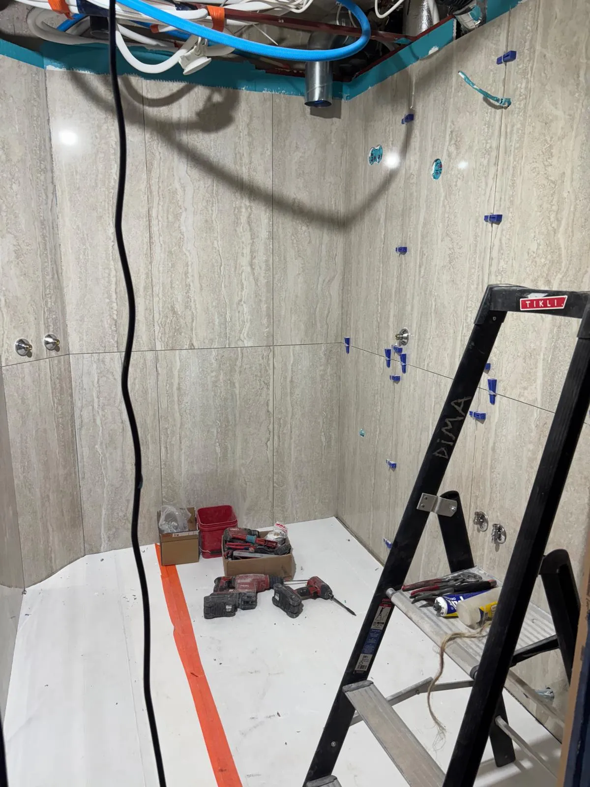 Valokuva keskeneräisestä kylpyhuoneesta, jossa on laatoitetut seinät, työkaluja lattialla ja tikkaat. Valoisa ja tilava.