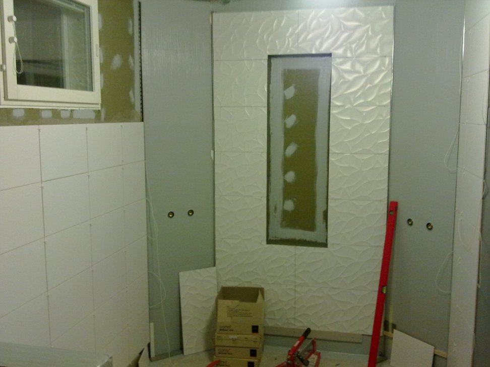 Keskeneräinen kylpyhuone, jossa on valkoiset laatat, ikkuna ja työkalut.