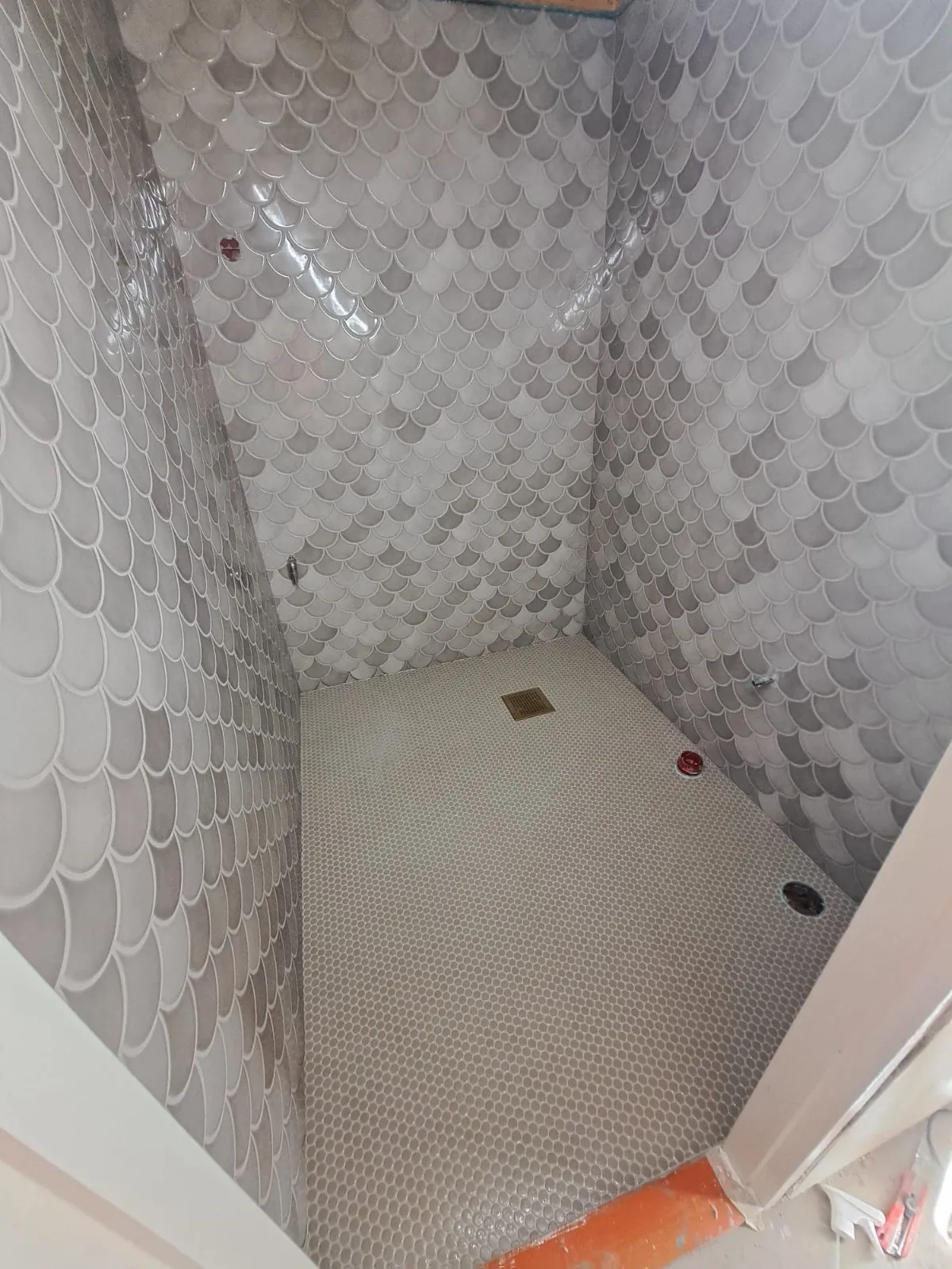 Kylpyhuoneen sisustus, jossa on harmaita kalanruotokuvioisia laattoja seinillä ja pieniä pyöreitä laattoja lattialla, luoden modernin ja tyylikkään ilmeen.