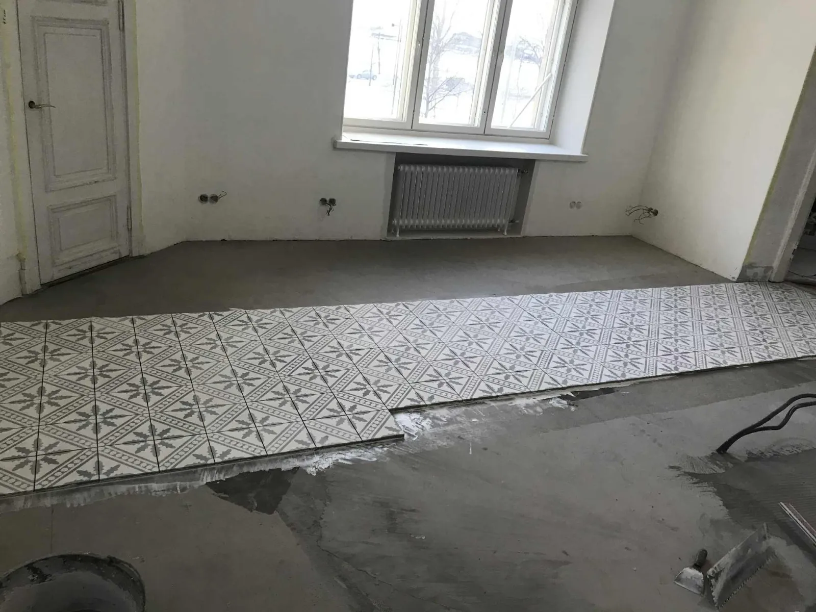 Huoneessa on asennettu kuvioituja lattialaattoja, ja lattia on osittain päällystetty harmaalla sementillä.