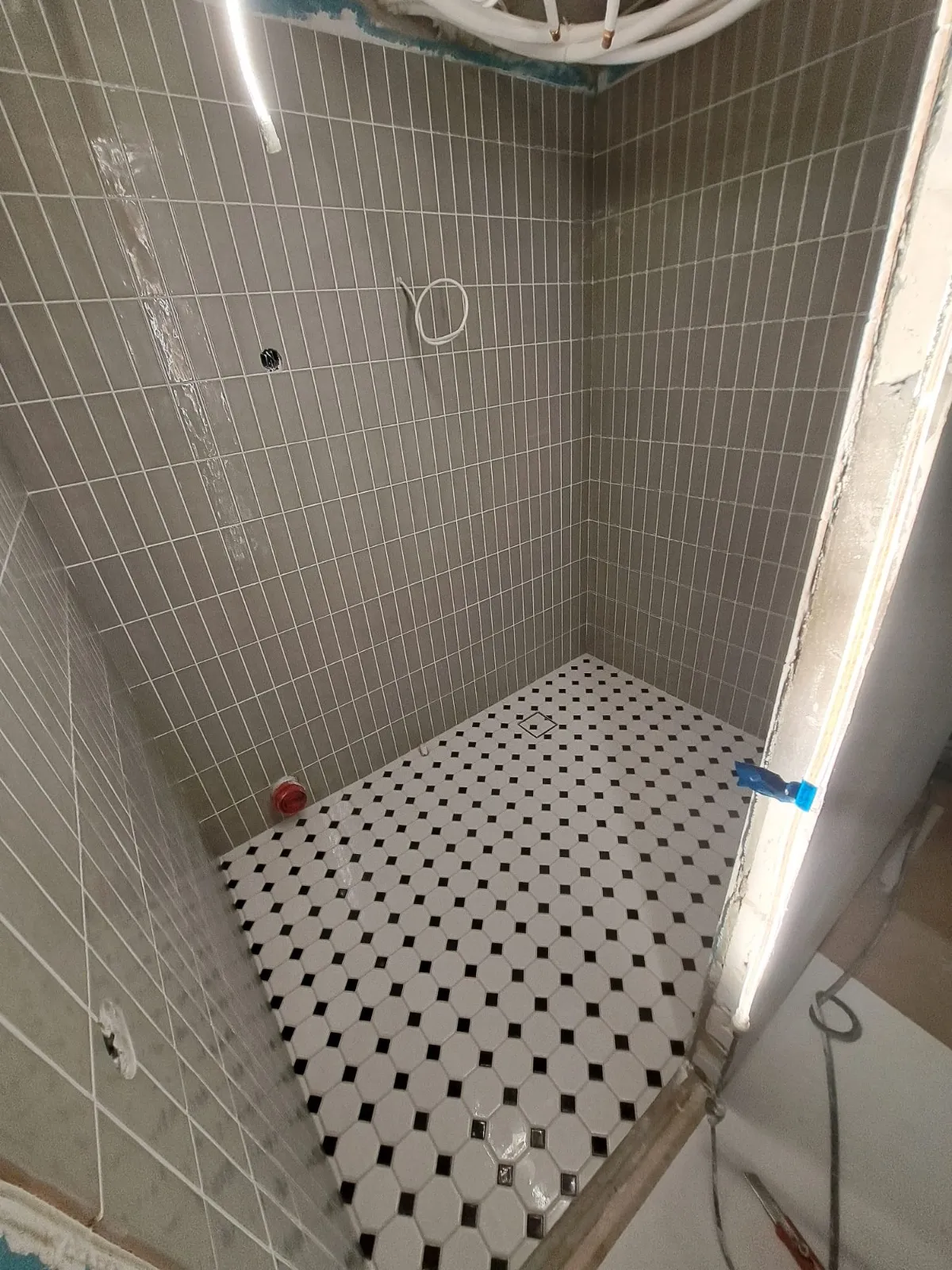 Harmaa laatoitettu suihkutila, jossa on mustavalkoinen mosaiikkilattia ja kirkas valaistus.