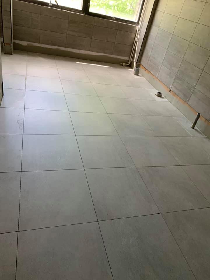 Huoneessa on harmaat laatat lattialla ja seinillä, ja valo tulee ikkunasta.