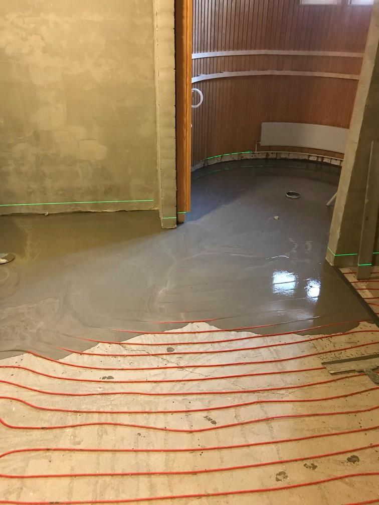 Huoneessa on lattialämmitysputket, osittain peitettynä tasoitekerroksella, ja seinät ovat osittain rapattuja.