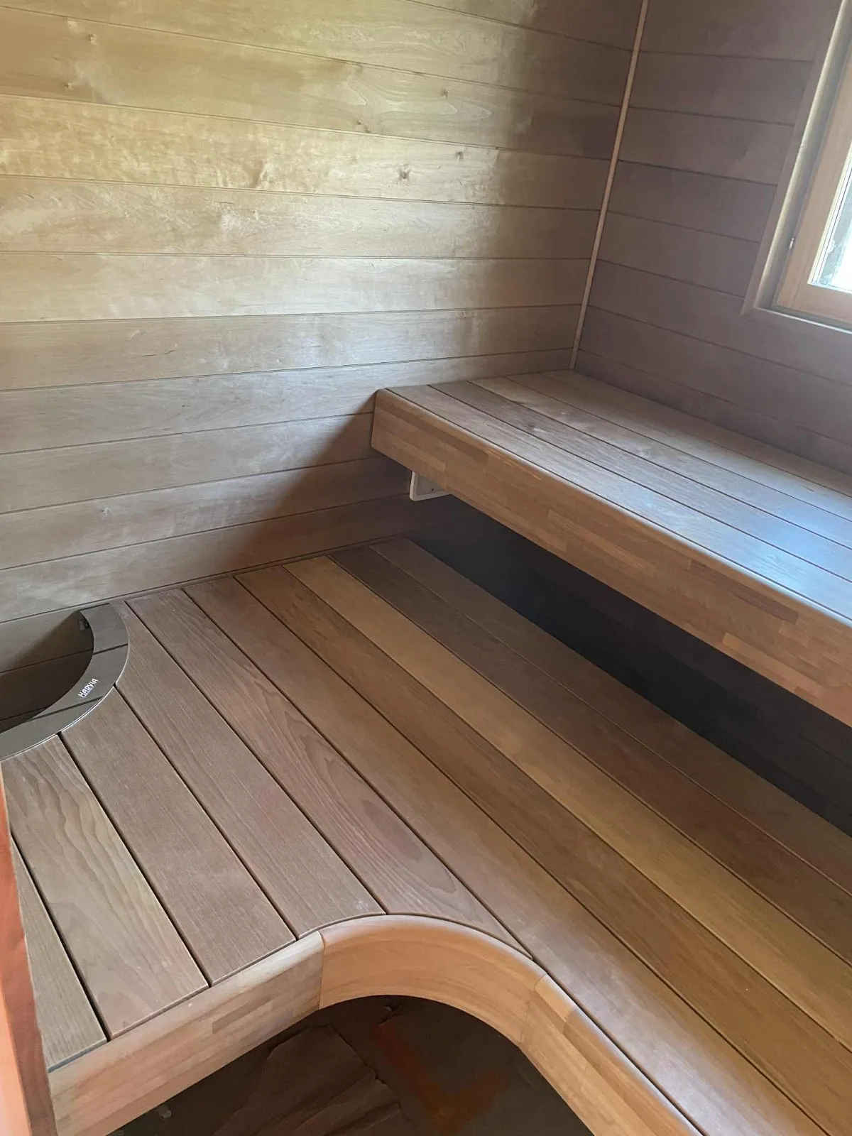 Puinen sauna, jossa on penkki ja lattia, luonnonvalossa.