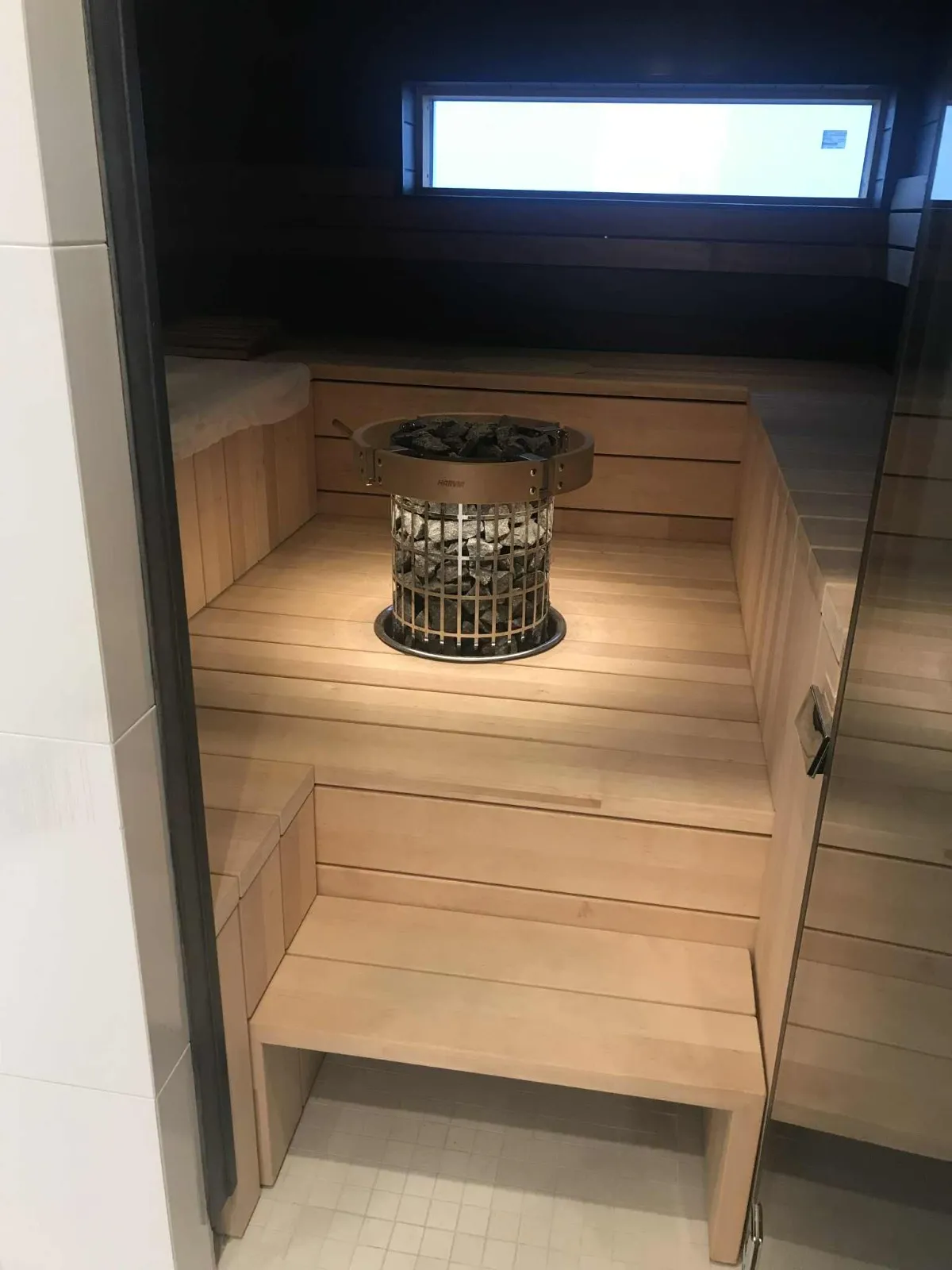 Saunan sisätila, jossa on puupaneelit, kivikiuas ja pieni ikkuna.