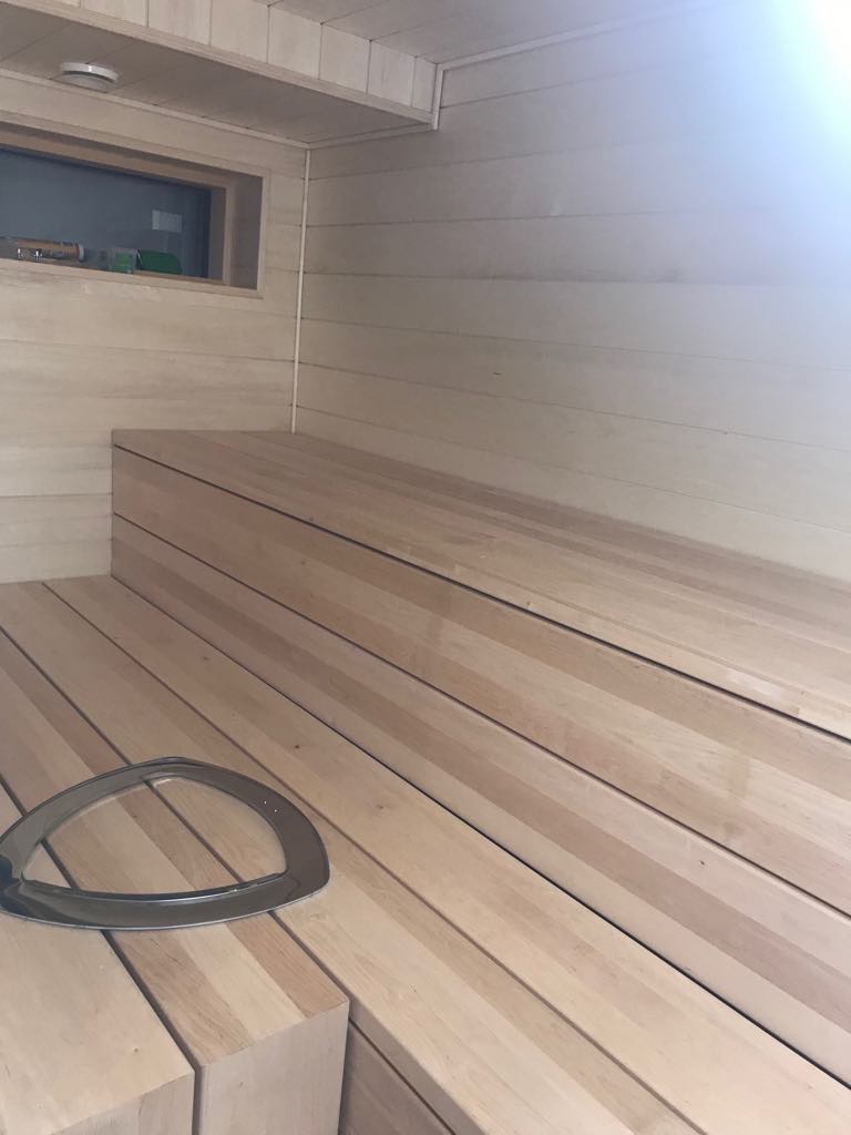 Vaalean puun sävyinen sauna, jossa on penkit ja metallinen kehys lattialla.