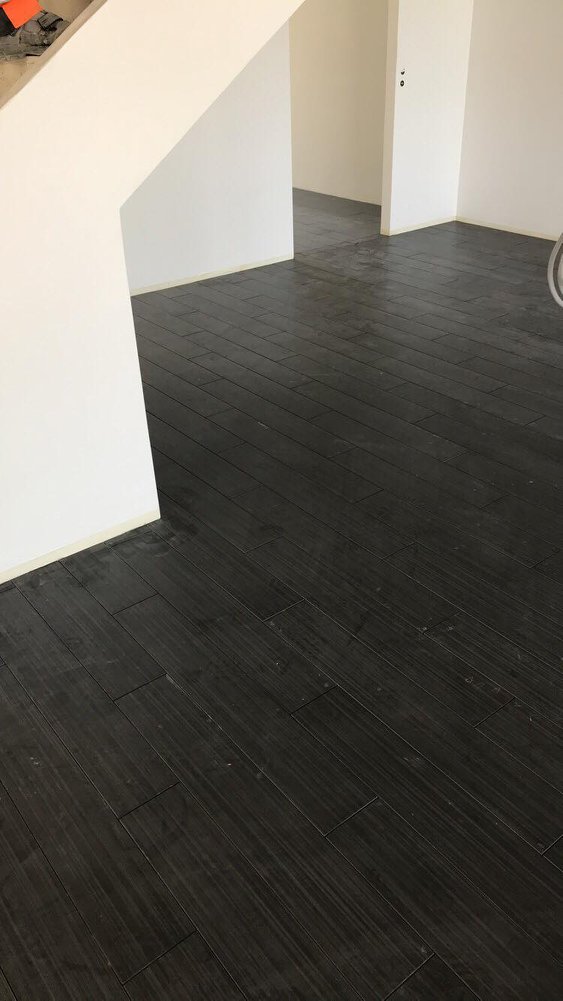 Sisätila, jossa on tumma puulattia, valkoiset seinät ja oviaukko. Lattia on asennettu vinosti, ja valo heijastuu sen pinnalta.